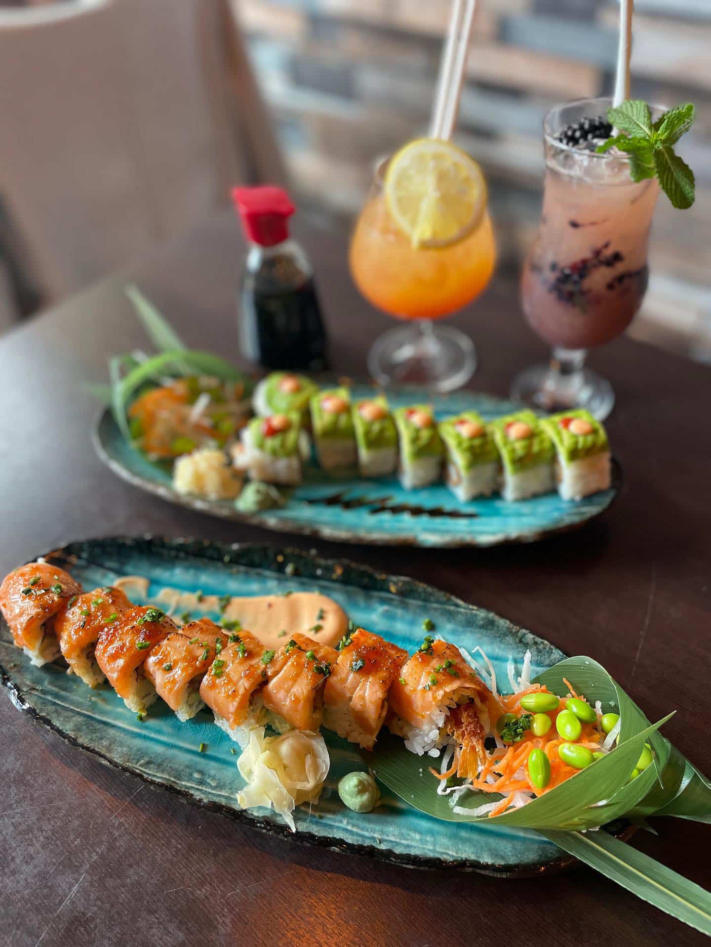 Two plates with sushi and drinks. One plate has a variety of sushi rolls, while the other has a selection of colorful beverages.