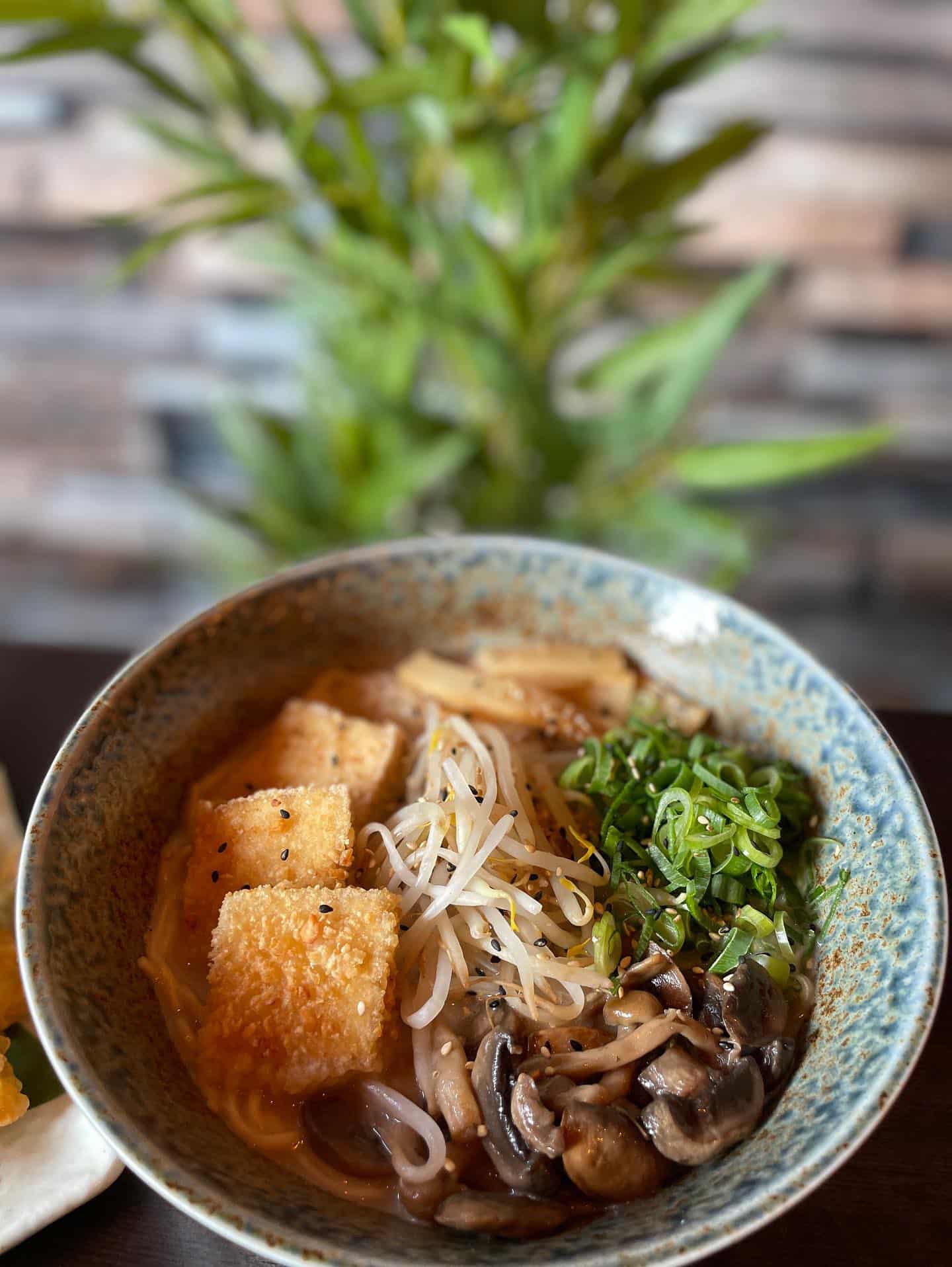 A bowl of ramen with tofu, mushrooms, and greens on the side.